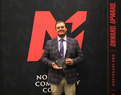 Shane Peterson holding award in front of Northeast Backdrop